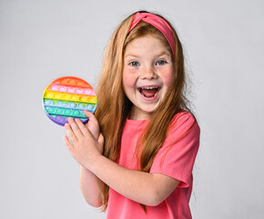 Portrait of happy screaming kid girl holding showing new sensory toy - pop it. Rainbow color,...