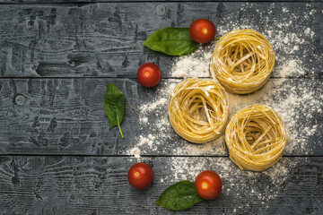 Tomatoes and rolled pasta on a wooden background. Space for the text.