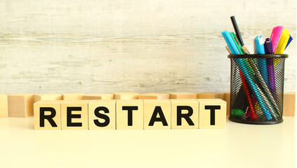 Seven stacked wooden cubes with letters RESTART on a white work table on a gray background.