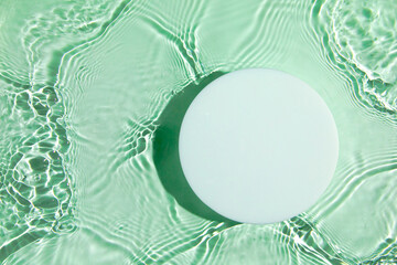 Empty white circle podium on transparent clear green calm water texture with splashes and waves in...