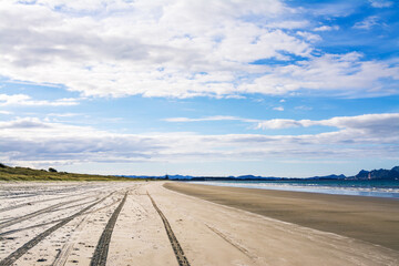 Tire tracks on an empty sandy beach go towards horizon