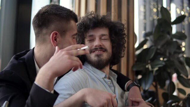 Male romanic gay couple in a cafe smoking a cigarette and cuddling, romantic lgbt couple concept