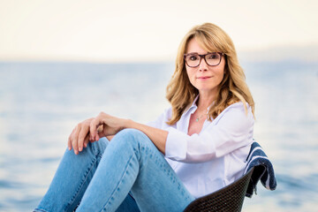 Fototapeta na wymiar Attractive middle aged woman wearing casual clothes while relaxing by the sea