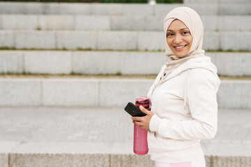 Middle eastern woman in hijab using mobile phone while working out