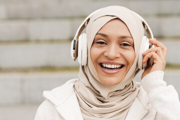 Middle eastern woman in hijab listening music with wireless headphones