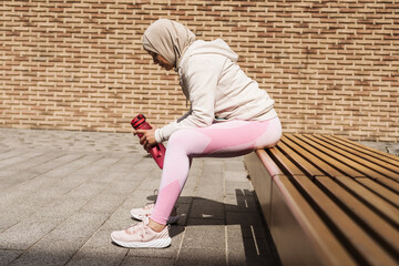 Middle eastern woman in hijab sitting on bench during workout