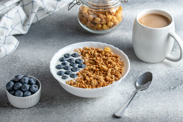 Granola with yogurt and coffee on a gray table. Hot morning drink. Muesli and blueberries in a white bowl. Dry breakfast concept. Healthy vegetarian food. Fitness diet.