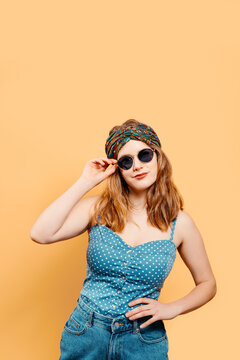 Young blonde girl with a bright headscarf looking at the camera wearing sunglasses with a denim top on a yellow background. summer concept. vertical image with copy space