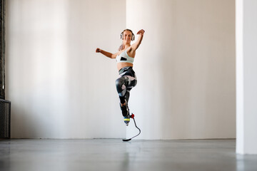 Young sportswoman with prosthesis listening music and dancing indoors - obrazy, fototapety, plakaty