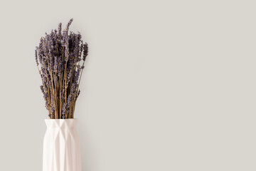 Bouquer of dry lavender flowers in white vase in front of gray background.