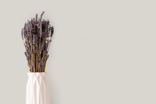 Bouquer of dry lavender flowers in white vase in front of gray background.