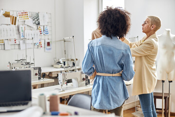 African-American stagist looks at mature lady fashion designer working with new jacket in workshop