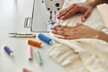 African-American seamstress sews white fabric with machine at workplace in studio