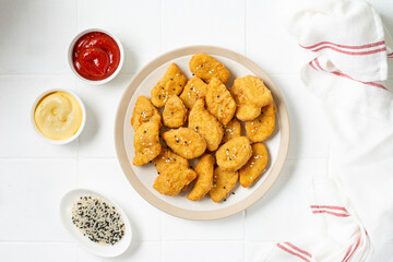 Chicken nuggets in a plate, ketchup and cheese sauce on a light background. Fast food top view