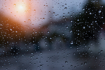 Water droplets on the windshield on the driver's side due to rain with a blurry background and an orange sun shining down on it.