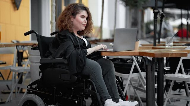 A beautiful disabled woman is using her laptop while sitting on the street cafe outside