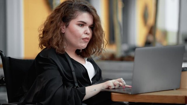 A positive disabled woman is using her laptop while sitting on the street cafe outside