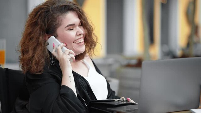 A happy laughing disabled woman is using her laptop while talking on her smartphone sitting on the street cafe outside