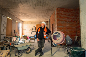 Builder engineer near concrete mixers. Foreman of construction team. Man in work uniform inside...