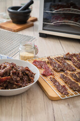 Asia Marinierte Rindfleisch Streifen roh für hausgemachtes Beef Jerky Trockenfleisch mit Sesam und Chili auf Edelstahl Trockengitter für Dörrautomat in Küche mit Holz Brett Hintergrund hell