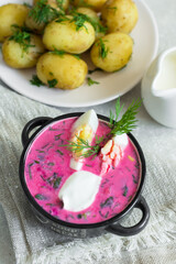 Traditional summer cold soup of beets, herbs, cucumber, eggs and sour cream, on a linen napkin, next to boiled young potatoes. Diet menu.
