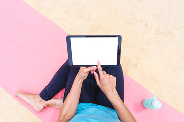 Screen mockup of fitness woman choosing an online sport class outdoors. Top view of young woman connecting with technology to a gym class outdoors at summer tropical retreat next to a swimming pool.
