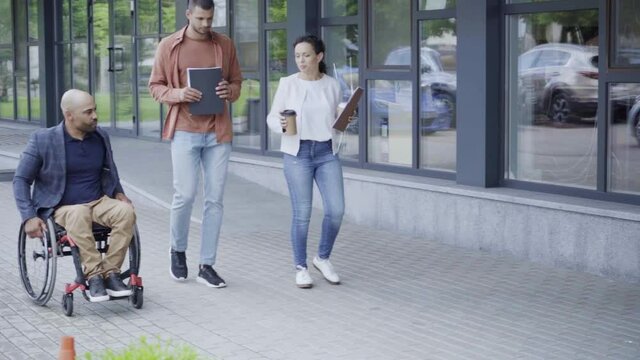 interracial people walking with handicapped african american boss near building