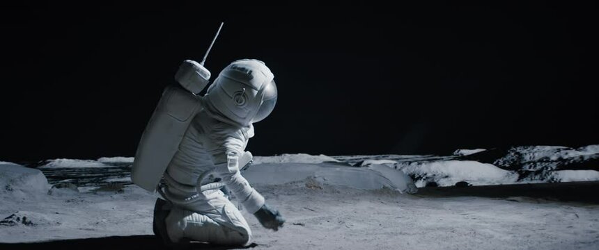 CU Portrait of Caucasian female lunar astronaut finds something and kneels while exploring Moon surface. Shot with 2x anamorphic lens