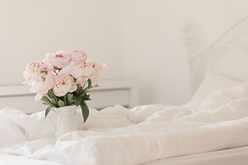 Fototapeta na wymiar Bouquet of pink peonies on white bed linen. Modern interior in the bedroom. Wedding and festive style.