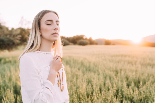 Calm female praying with cross in field
