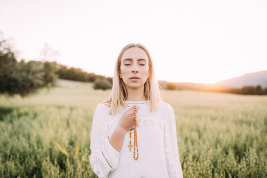 Calm female praying with cross in field