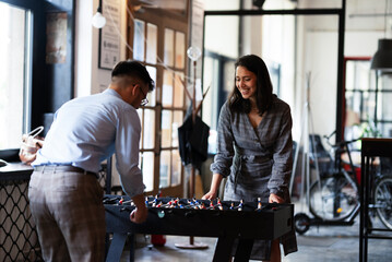 Colleagues having fun at work. Businessman and businesswoman playing table soccer..