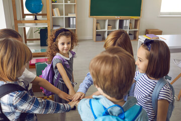 Team of school children joining hands standing in circle in modern classroom. Bunch of cute kids having bonding moment with friends, feeling united and supported. Peer group, community, unity concept