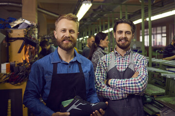 Portrait of happy smiling shoemakers looking at camera standing together over workshop interior....