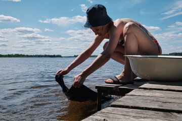 Young girl washes clothes by hand in lake.