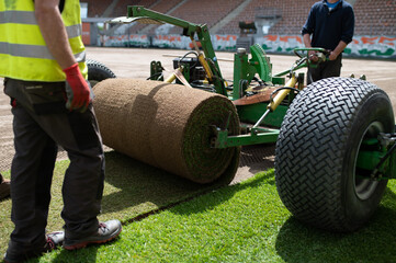 Workers laying grass in a roll on a professional football field.