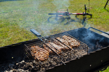 Four large pieces of pork are crispy on a charcoal grill. In the background there is a bicycle...