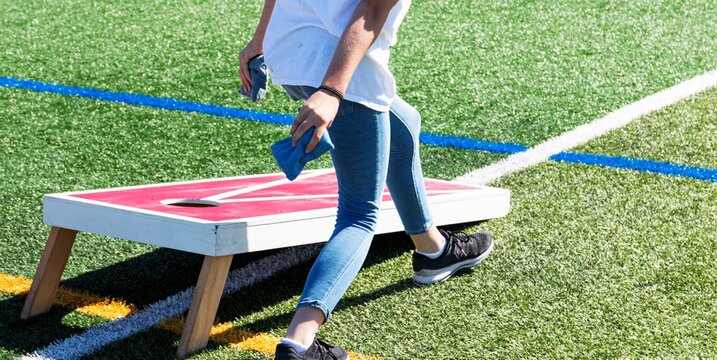 Person throwing a bean bag while playing cornhole on a turf field