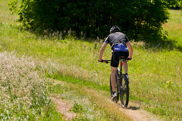 Fototapeta premium Summer bike ride in nature. A cyclist rides on a country road. Selective focus.