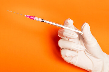 Hand in white gloves holding syringe on oragne background with copy space