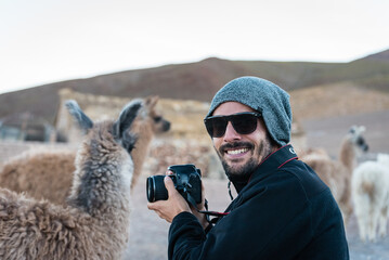 Young man with his camera smiles next to a llama