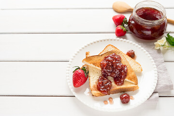 Toasted bread slices with strawberry jam and a jar of jam