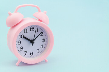 Pink alarm clock on blue background, large space for text.	