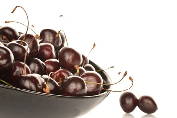 Several ripe organic cherries in a black ceramic plate, close-up, isolated on white.