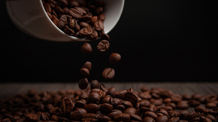 A close-up of coffee beans spilling from a white cup, creating a rich texture against a dark background, perfect for coffee lovers.