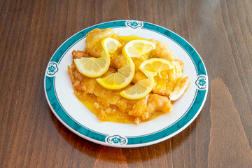 Breaded chicken fillets soaked in Chinese lemon sauce on white plate and brown wooden table