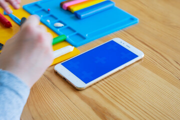 Children's hands during modeling from plasticine, mobile phone with chroma key blue screen. Space for text