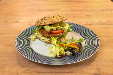 Fantastic vegan lentil burger with guacamole, pickles, tomato, lettuce, piparra, black olives and cherry tomatoes on a beautiful plate