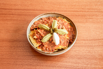 Bowl of corn nachos soaked in spicy chili con carne topped with guacamole and cream cheese