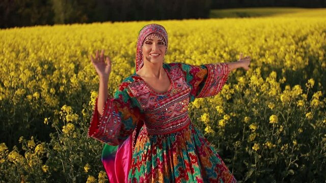 Young woman in national Afghan costume dancing in a field with yellow rapeseed flowers